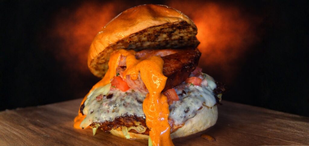 Hamburguesa Fresh & Furious con pan brioche de patata, carne de retinto, queso Edam, lechuga Batavia, pico de gallo y bacon, cubierta con salsa Yogui secreta; primer plano con la salsa cayendo.